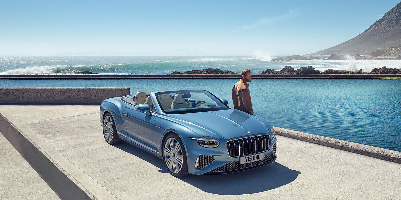 Bentley Al Khobar New Bentley Continental GTC Azure convertible front view in Light Windsor blue paint with 22 inch ten spoke wheels parked by the sea in the sunshine
