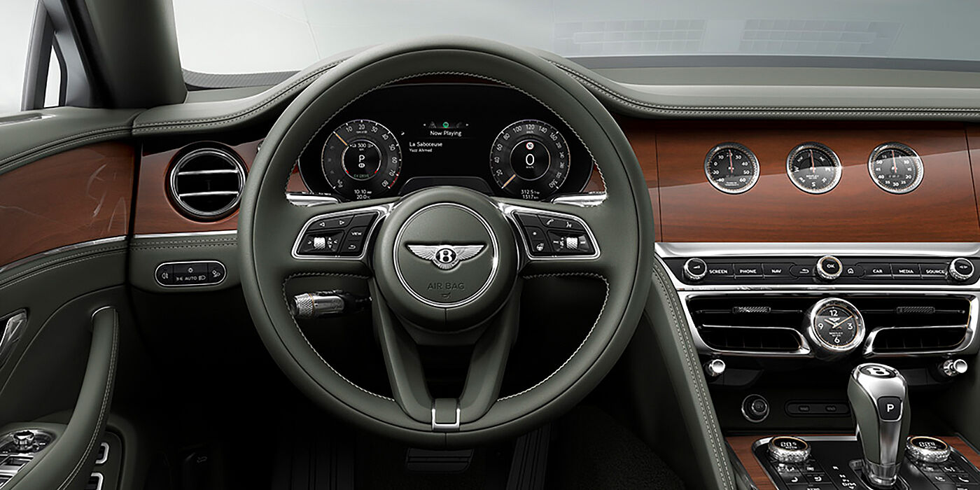 Bentley Al Khobar New Bentley Flying Spur sedan front cabin in Cumbrian Green hide and Crown Cut walnut veneer showing steering wheel and Rotating Display with three clocks on face