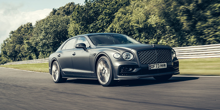 Bentley Al Khobar Bentley Flying Spur Mulliner sedan front three quarter in dark grey paint driving dynamically by some trees on a track
