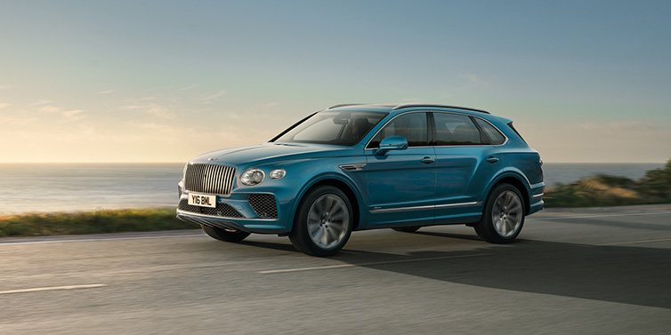 Bentley Al Khobar Bentley Bentayga Azure SUV in Topaz blue paint driving dynamically by the ocean with 22 inch 10 spoke directional wheels