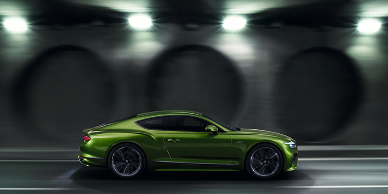 Bentley Al Khobar Bentley Continental GT Speed coupe profile in Tourmaline Green driving dynamically past a concrete wall at night