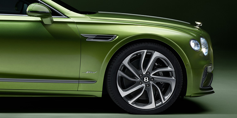 Bentley Al Khobar Bentley Flying Spur Speed sedan exterior close up in Tourmaline Green paint with chrome B wing vent, chrome Speed badge and 22 inch ten swept spoke wheel