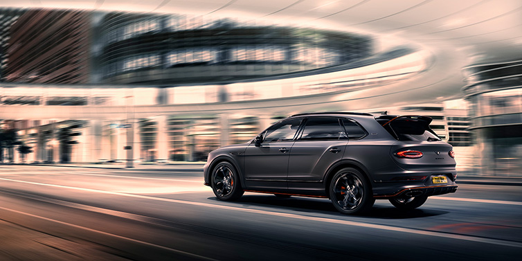 Bentley Al Khobar Bentley Bentayga S Black Edition SUV rear three quarter in Anthracite Satin paint driving dynamically through a city at night