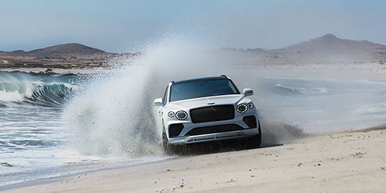 Bentley Al Khobar Bentley Bentayga Speed SUV facing front in Snow Quarts Pearlescent white paint driving dynamically on beach