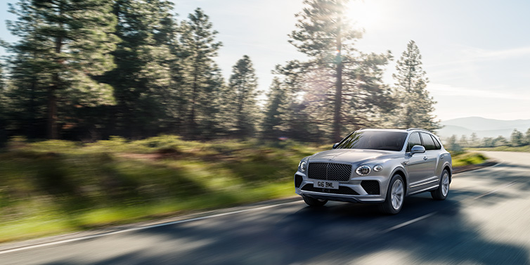 Bentley Al Khobar Bentley Bentayga SUV front three quarter in Moonbeam silver paint driving dynamically along a tree-lined road