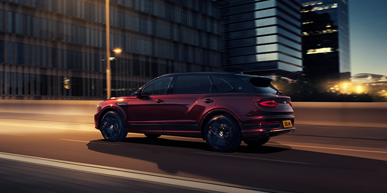Bentley Al Khobar Bentley Bentayga Extended Wheelbase Mulliner SUV in Cricket Ball red paint driving dynamically in city at night