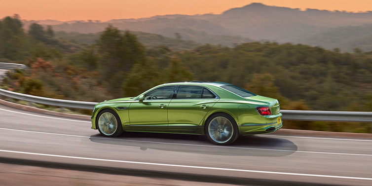 Bentley Al Khobar Bentley Flying Spur Speed sedan side profile in Tourmaline Green paint driving dynamically on a mountain road at sunset