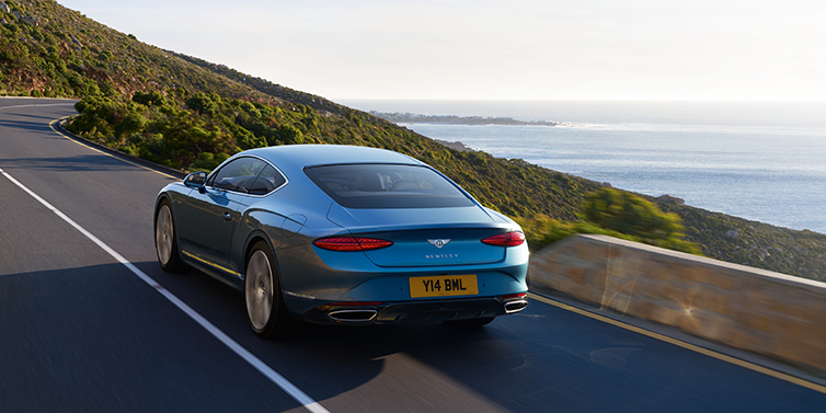 Bentley Al Khobar New Bentley Continental GT Azure coupe in Light Windsor blue paint seen from the rear driving dynamically on a seaside road
