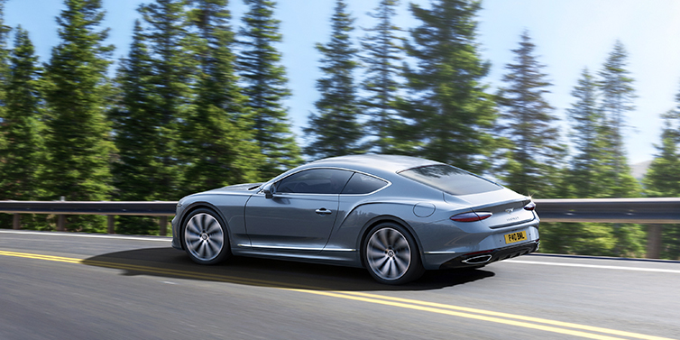 Bentley Al Khobar New Bentley Continental GT coupe in Silverlake paint, seen from the rear, driving dynamically on a tree-lined road