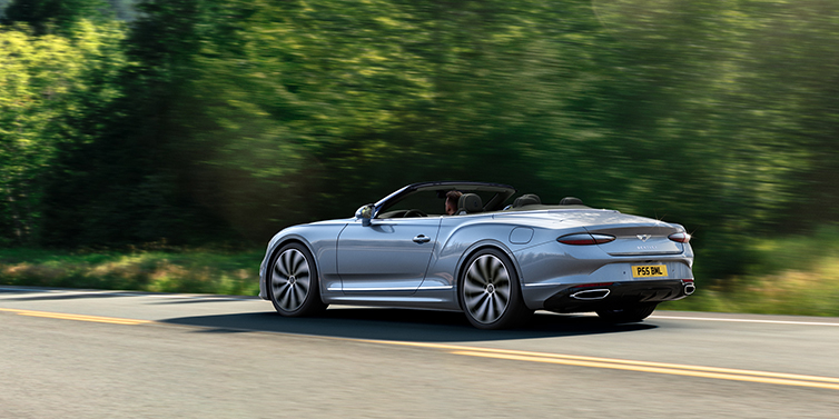 Bentley Al Khobar New Bentley Continental GTC convertible side view in Silverlake paint with 22 inch ten spoke wheels driving dynamically on a country road