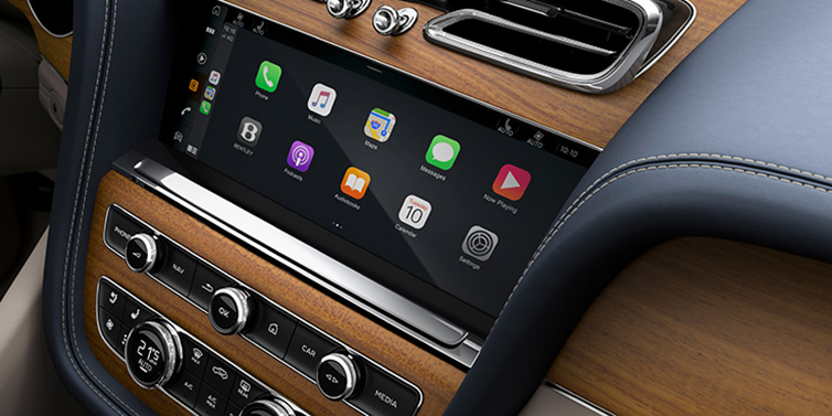 Bentley Al Khobar Bentley Bentayga Azure SUV front interior console with MMI screen showing apps, surrounded by Imperial Blue and Portland hides, and Open Pore Koa veneer